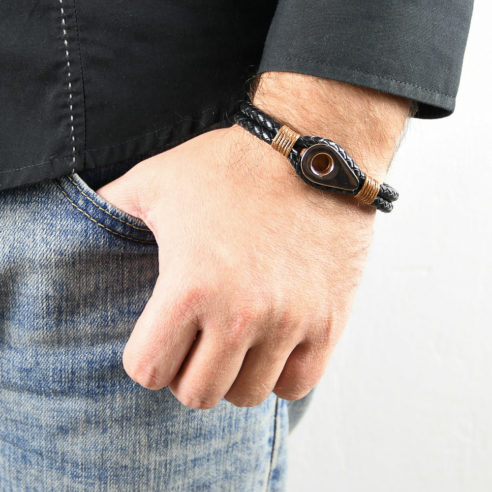 Bracelet pour homme en cuir noir tressé avec une poulie de couleur or rose et des cordages ocre de part et d'autre.